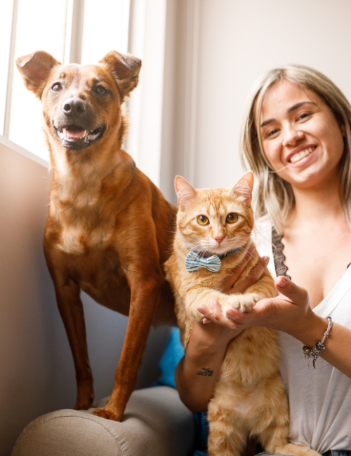 A woman sits on a couch with her dog and cat